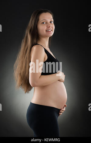 Portrait der junge Schöne schwangere Frau auf schwarzem Hintergrund Stockfoto