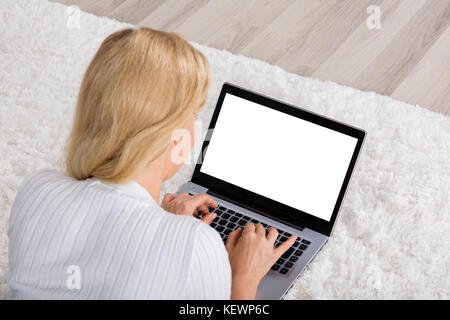 Hohe Betrachtungswinkel von Frau mit Laptop zeigt leeren Bildschirm auf dem Teppich liegend Stockfoto