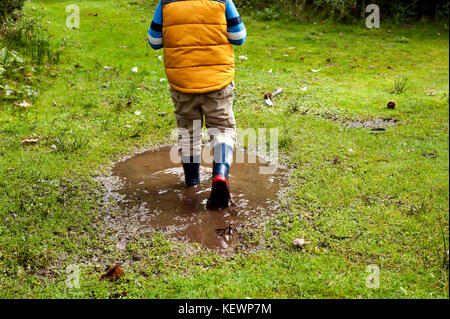 Junge Spaß Spritzwasser in schlammigen Pfützen Stockfoto