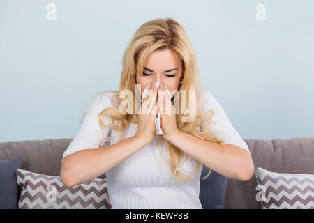 Porträt einer jungen Frau mit Allergie oder Grippe Nase weht in Seidenpapier auf der Couch. Stockfoto