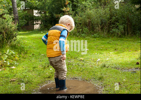 Junge Spaß Spritzwasser in schlammigen Pfützen Stockfoto