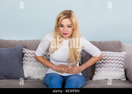 Junge unglückliche Frau leidet unter Bauchschmerzen auf der Couch zu Hause Stockfoto