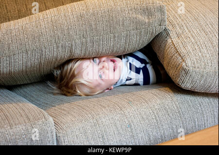 Kleiner Junge versteckt sich unter Sofakissen Stockfoto