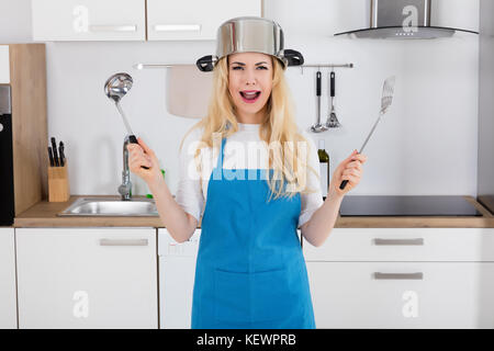 Porträt einer frustrierten Frau tragen Kochpfanne holding Löffel in der Küche zu Hause. Stockfoto
