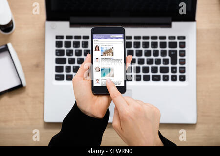 Nahaufnahme einer Geschäftsfrau, die Hand mit Social Networking Website auf Handy im Büro Schreibtisch Stockfoto