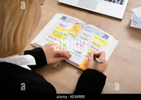 Hohe Betrachtungswinkel und einer Geschäftsfrau Schreiben Zeitplan im Tagebuch auf hölzernen Schreibtisch Stockfoto
