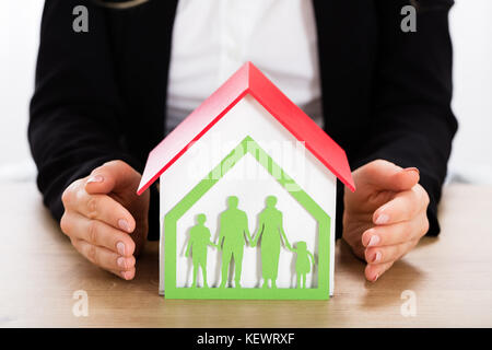 Geschäftsfrau Schutz Haus Modell mit papercut Familienhaus auf hölzernen Schreibtisch Stockfoto