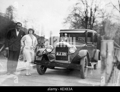 Dieses Foto zeigt ein Doppelporträt einer Person und eines Autos auf einer Brücke. Das Auto, wahrscheinlich von amerikanischer Marke, hat ein sichtbares Nummernschild. Das Bild zeigt die Automobilkultur des frühen 20. Jahrhunderts und die Schnittstelle zwischen Transport und persönlicher Porträtarbeit. Stockfoto