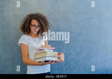 Portrait von jugendlichen Mädchen mit Brille steht neben der Wand und hält mehrere Bücher Stockfoto