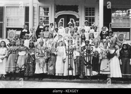 Dieses Foto zeigt eine Gruppe festlich gekleideter Kinder, die mit mehreren Missionaren posieren. Das Bild ist Teil der Sammlung des National Museum of World Cultures und spiegelt kulturelle Interaktionen in historischen Zusammenhängen wider. Stockfoto