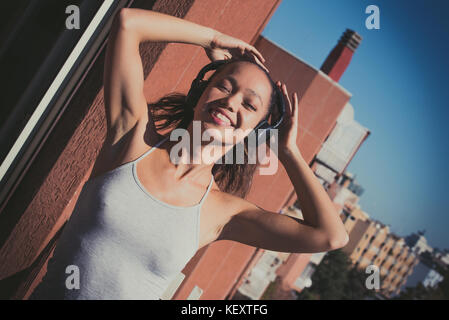Jungen asiatischen Teenager Frau Outdoor Portrait geschlossenen Augen Sonnenlicht lächelnd mit Kopfhörer portrait Stockfoto