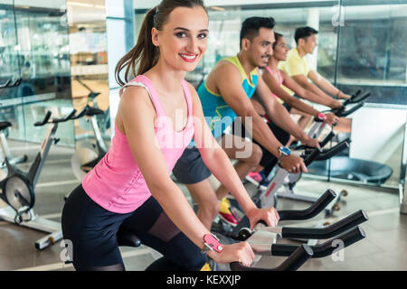 Schöne passende Frau während cardio Workout lächelnd an Indoor cycl Stockfoto