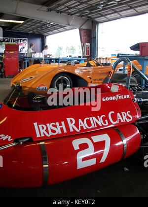 Watkins Glen Rennwagen Garagenszene mit einem leuchtend roten Formel Rennwagen vor einem Orange McLaren Can-am Rennwagen. Stockfoto