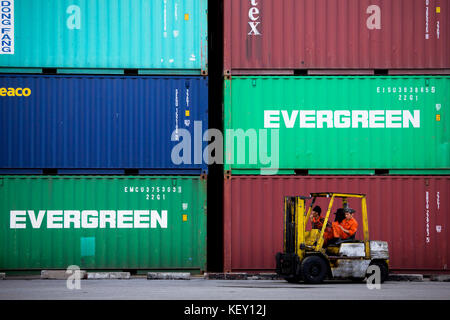 Hafenarbeiter ruhen nach der Arbeit im Hafen auf einem Gabelstapler, während die Frachtcontainer auf den Transport der Exportschifffahrt warten. Stockfoto