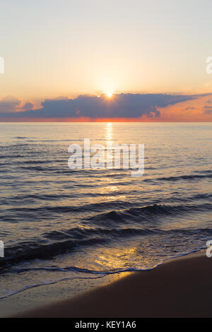 Majestic Sonnenaufgang am Meer Strand Meer Wellen drehen golden, wenn die Sonne durch die Wolken am Morgen erscheint. Stockfoto