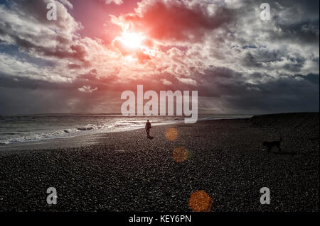 Mann in Silhouette entlang ein Kiesstrand mit dramatischen Himmel Stockfoto