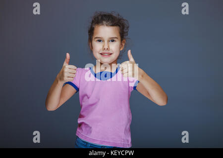 Kleines Mädchen zeigt Zeichen 'Ja' Finger auf grauem Hintergrund Stockfoto