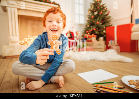 Aufgeregt rothaarige Junge grinste breit und zeigt hausgemachte Gingerbread Man Stockfoto