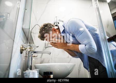 Reifer Geschäftsmann in einem Hotelzimmer-Badezimmer. Gutaussehender Mann, der sein Gesicht wäscht. Stockfoto