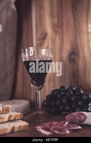 Ein Glas Rotwein, Weintrauben, getrocknete Wurst, Brot und Käse Brie Stockfoto