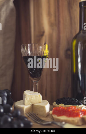 Ein Glas Rotwein, Brie Käse, Trauben und Kaviar, geringe Tiefenschärfe Stockfoto