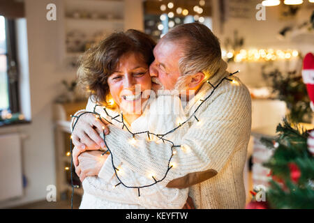 Schönes älteres Ehepaar in weißen wollenen Pullover zu Hause umarmte. Mann und Frau Spaß zu Weihnachten. Stockfoto