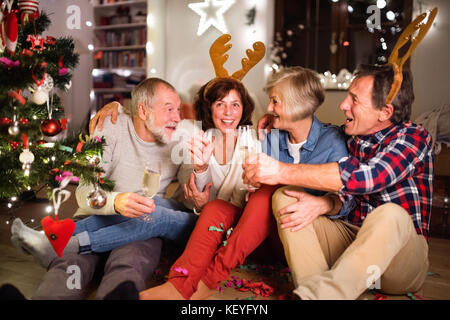 Ältere Freunde tragen zu Weihnachten Stirnbänder mit Rentiergeweih, trinken Wein und haben Spaß. Stockfoto