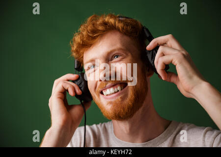 Junge curly Abtastkopf bärtiger Mann genießt Musik hören, über grüne Hintergrund Stockfoto