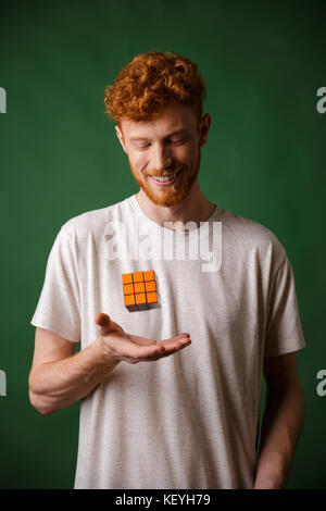 Der junge lächelnde Abtastkopf bärtiger Mann, Rubik's Cube, über grüne Hintergrund Stockfoto