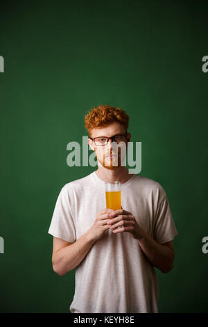 Portrait einer jungen rothaarigen Mann hält ein Glas Bier, während über grüne Hintergrund isoliert Stockfoto