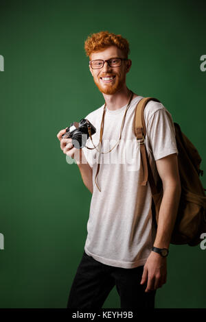 Portrait von lächelnden Abtastkopf bärtigen Hipster mit retro Kamera und Rucksack, auf grünem Hintergrund Stockfoto