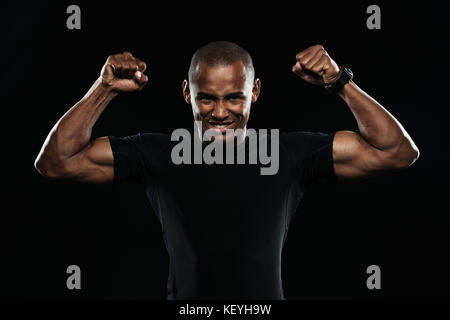 Junge glücklich Afro American Sports Mann seinen Sieg feiern mit erhobenen Armen, in die Kamera schaut, auf schwarzem Hintergrund Stockfoto