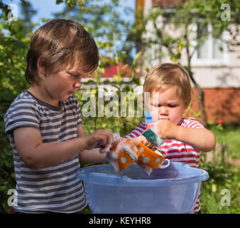 Zwei kleine Jungen helfen Gerichte im Freien im Dorf zu waschen, im Land. Konzentrieren Sie sich auf die Schale Stockfoto