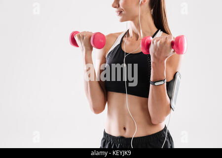 Zugeschnittenes Bild eines motivierten fitness Frau in Sportswear Hören von Musik über Kopfhörer während der Übungen mit Hanteln über Weiß ba isoliert Stockfoto