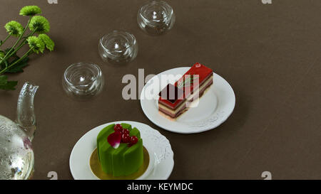 Schöner transparenter Teekanne mit leckerem grünem schwarzem Tee mit Apfel, mit Kerzen und mit Dessert im Hintergrund. Türkischer Tee in traditionellem Glas auf Holztisch. Kuchen und Teekanne aus Glas Stockfoto