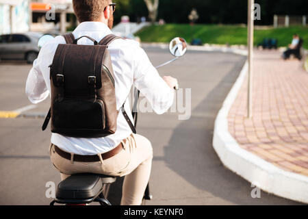 7/8 Rückansicht der Mann mit Rucksack reitet auf modernen Motorrad draußen Stockfoto