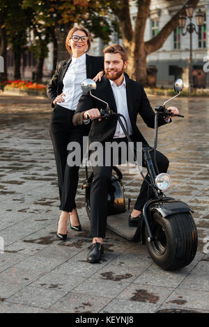 Volle Länge Bild von Happy business Paar posiert mit modernen Motorrad draußen, und wenn man die Kamera Stockfoto