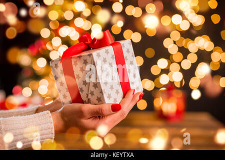 Detail der Frau hand Weihnachtsgeschenk mit blur Lichtpunkte um. Feier von Weihnachten, gemütliche Atmosphäre Stockfoto