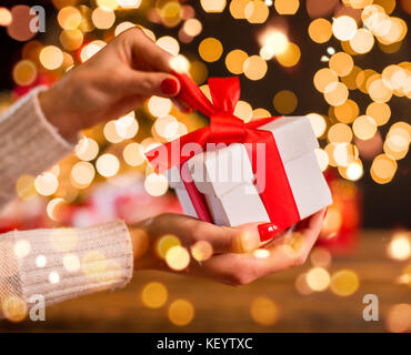 Detail der Frau Hand auspacken Weihnachtsgeschenk mit blur Lichtpunkte um. Feier von Weihnachten, gemütliche Atmosphäre Stockfoto