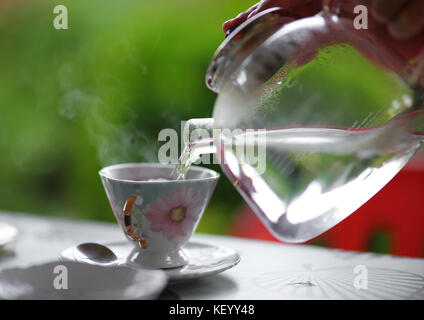 Strömenden heißen Wasser aus Glas Teekanne in die Tasse Tee, Außenpool im Sommer Stockfoto