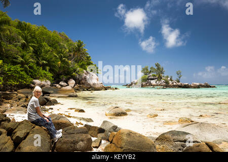 Die Seychellen, Praslin, Anse Royale, Ile Souris, Strand, älteren Touristen auf Granitfelsen sat Stockfoto