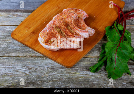 Rohes Schweinefleisch Steaks auf Holzbrett mit Kräutern, Knoblauch, Gewürze, Tomaten und bereit für das Kochen. Selektive konzentrieren. Stockfoto