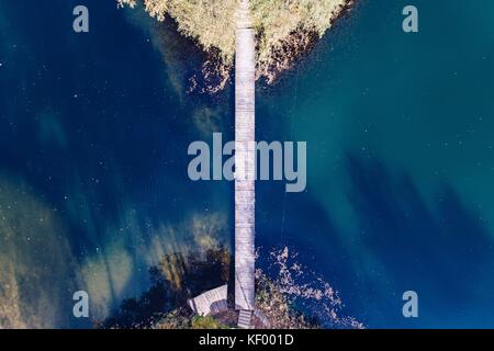 Antenne drone Ansicht auf zwei kleine Inseln auf dem See durch kleine Holzbrücke verbunden. Herbst am See Stockfoto