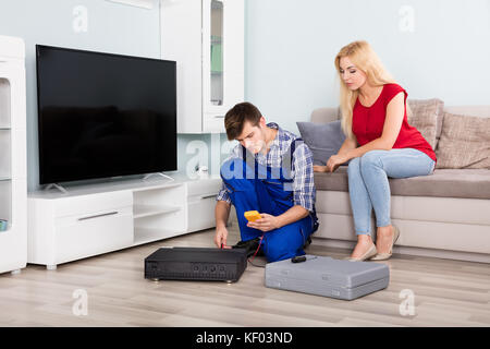 Frau sitzt auf der Couch bei männlichen Techniker installieren tv Box zu Hause Stockfoto