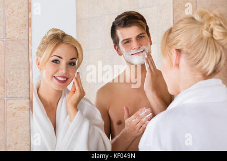 Porträt eines Mannes, Rasieren und Ihrer Frau Reinigung Ihr Gesicht im Spiegel zu Badezimmer Stockfoto
