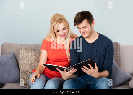 Junge glückliches Paar Nebeneinander sitzen auf dem Sofa bei Foto Album suchen Stockfoto
