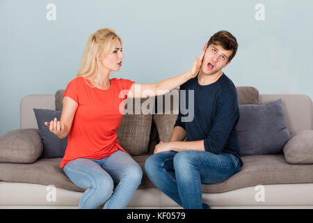 Wütende Frau Auf Der Couch, Die Ihren Mann Schlug, Während Sie Sich Über Untreue Und Scheidung Zu Hause Stritt Stockfoto