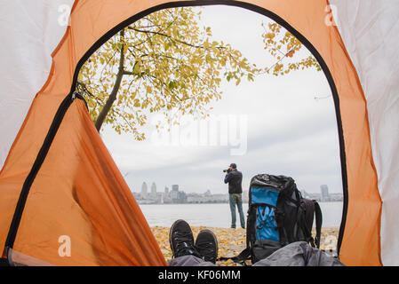 Blick aus dem Zelt mit Beinen. Beine in einem Zelt mit einer schönen Aussicht außerhalb. Silhouette eines Mannes Bilder aufnehmen am Ufer. Konzentrieren Sie sich auf Schuhe. a b Stockfoto