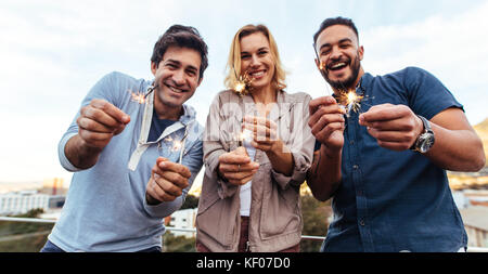 Gruppe von Freunden genießen Sie auf der Dachterrasse Party mit Wunderkerzen. Tausendjährige Gruppe von Freunden holding Wunderkerzen auf der Dachterrasse bei Sonnenuntergang. Stockfoto