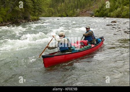 Zwei Männer navigieren Sie mit einem Kanu durch rauschende Stromschnellen während ein Abenteuer auf einem wilden Alaskan River. Stockfoto